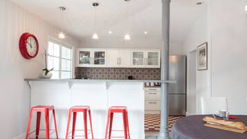 Una cocina moderna con armarios blancos, un reloj rojo y tres taburetes rojos.