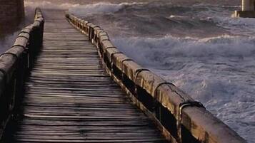 A wooden pier extending into rough waters, with a sturdy railing on both sides.