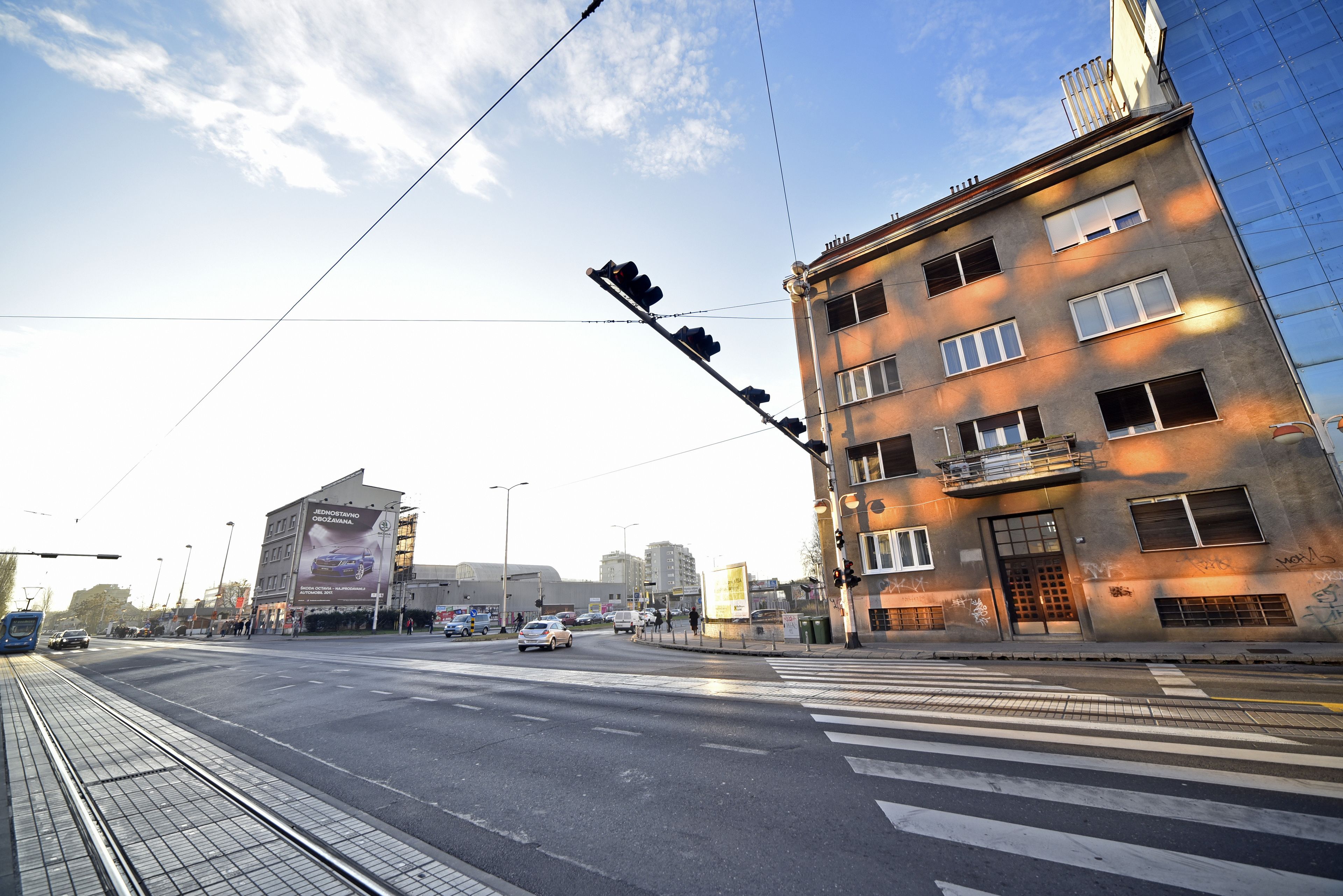A city intersection with a tram line, buildings, and a clear sky.