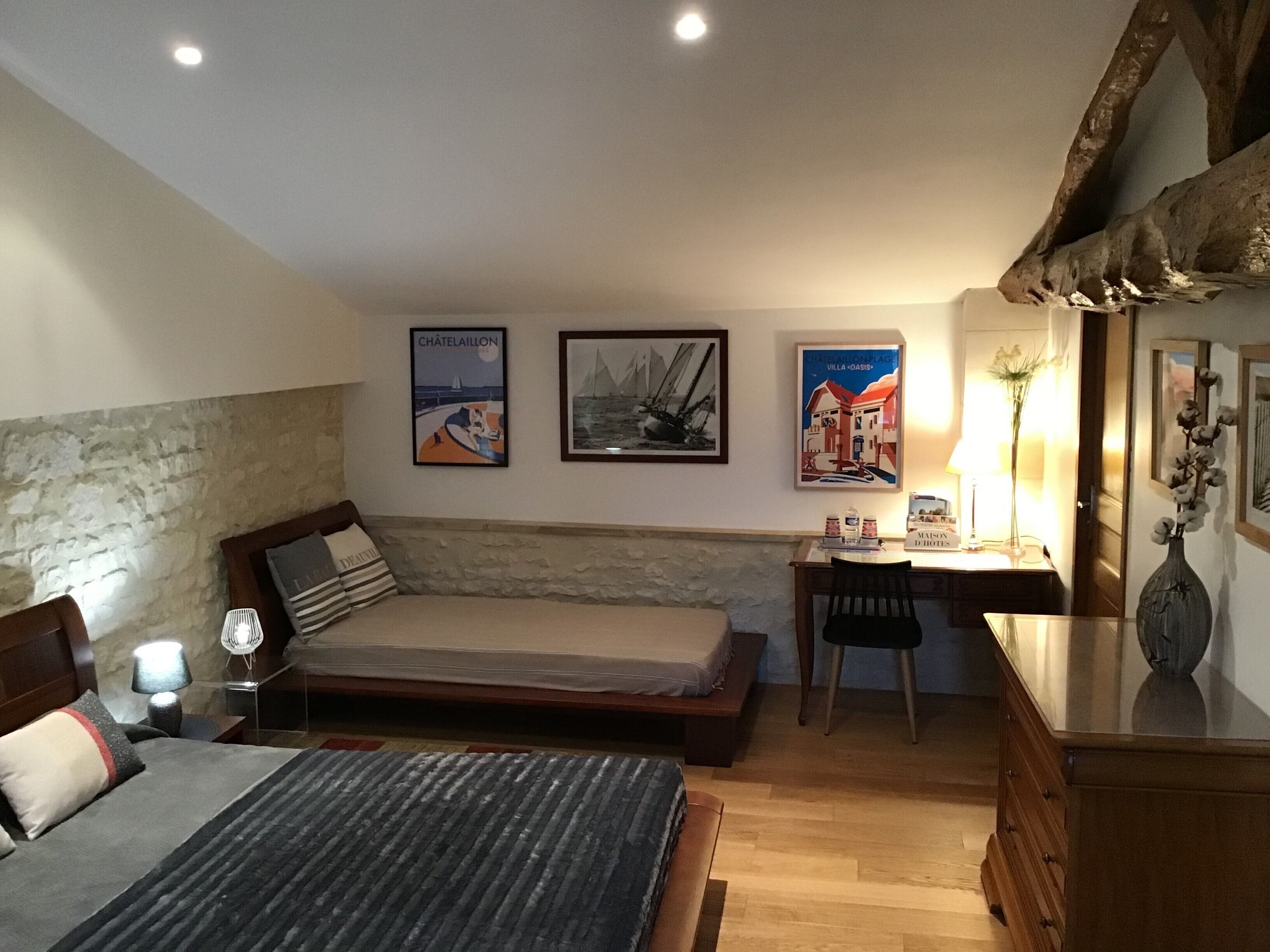 A bedroom with a bed, a desk, and a chair. There are three framed pictures on the wall.