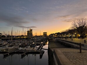 Un puerto deportivo con barcos amarrados, una estructura similar a un castillo y un paseo pavimentado junto al agua.