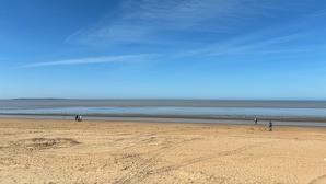 A wide beach with a clear sky, calm sea, and a few people walking. - L'Escale de Mortagne (Thairé)