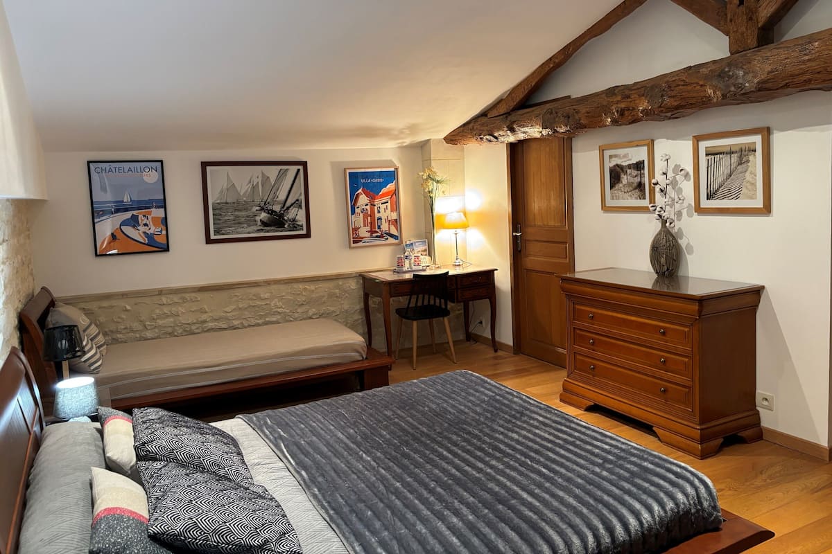 A bedroom with a bed, a desk, a dresser, and a wooden ceiling beam.