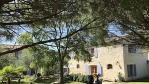 A stone building with a garden, a large tree, and a clear blue sky. - L'Escale de Mortagne (Thairé)