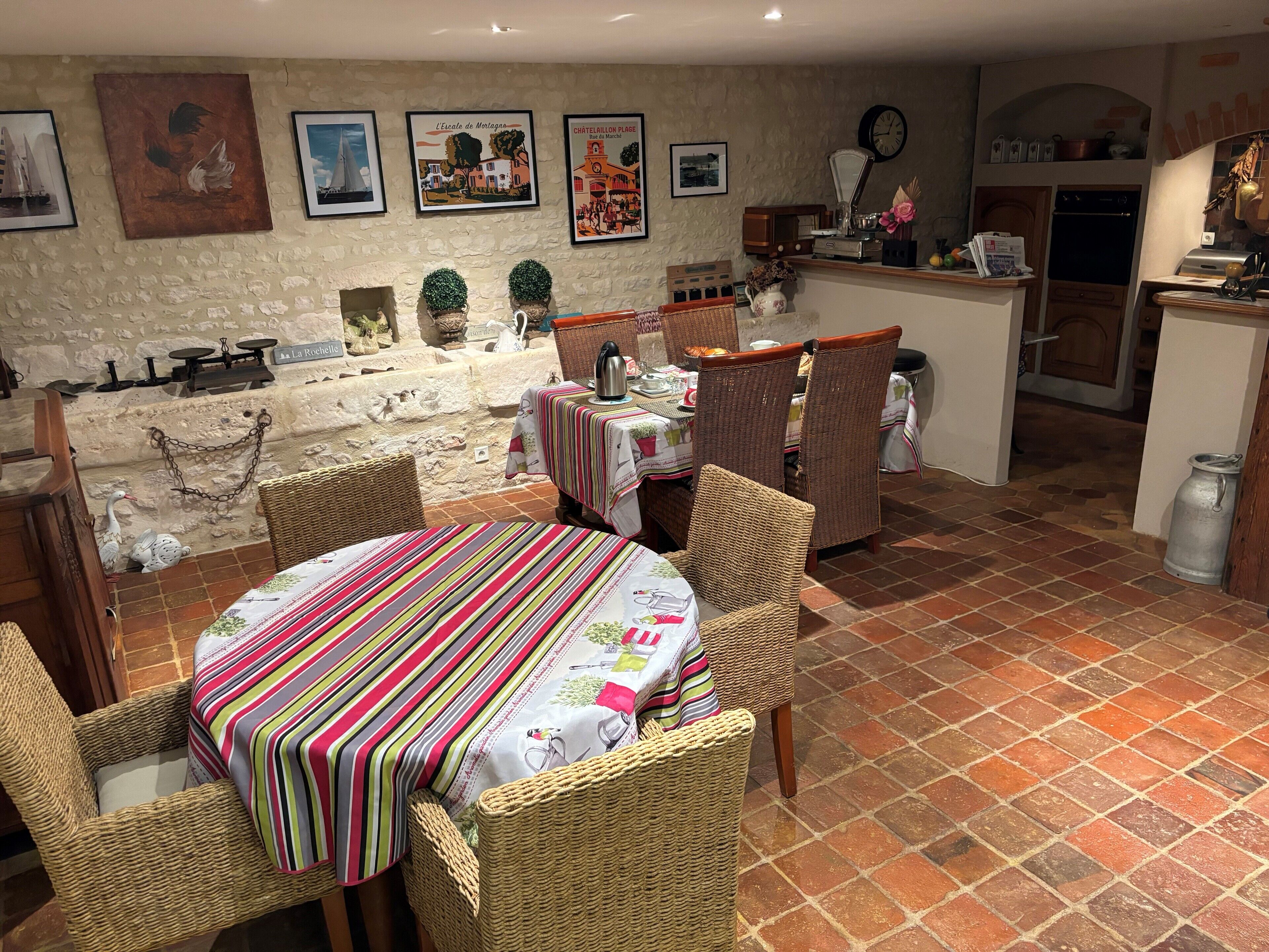 A dining area with wicker chairs, a round table with a striped tablecloth, and a kitchen in the background.