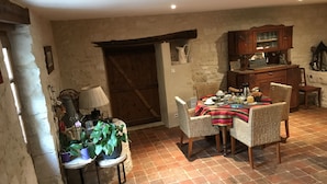 A rustic dining area with a brick floor, a wooden door, and a dining table set with plates, cups, and a striped tablecloth. - L'Escale de Mortagne (Thairé)