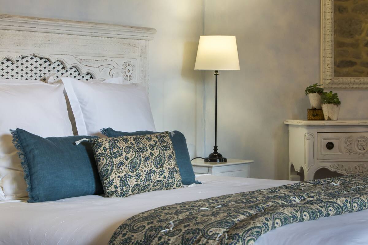 A neatly made bed with patterned bedding, a bedside lamp, and a dresser with decorative elements.