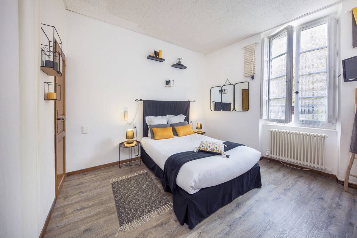 A bedroom with a bed, bedside tables, a window, a radiator, and a mirror on the wall.