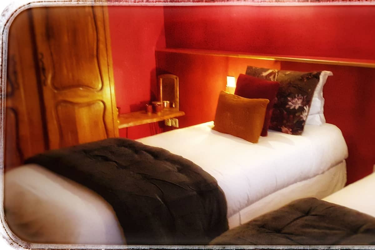 A hotel room with two beds, a nightstand, a mirror, and red walls.