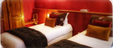 A hotel room with two beds, a nightstand, a mirror, and red walls.