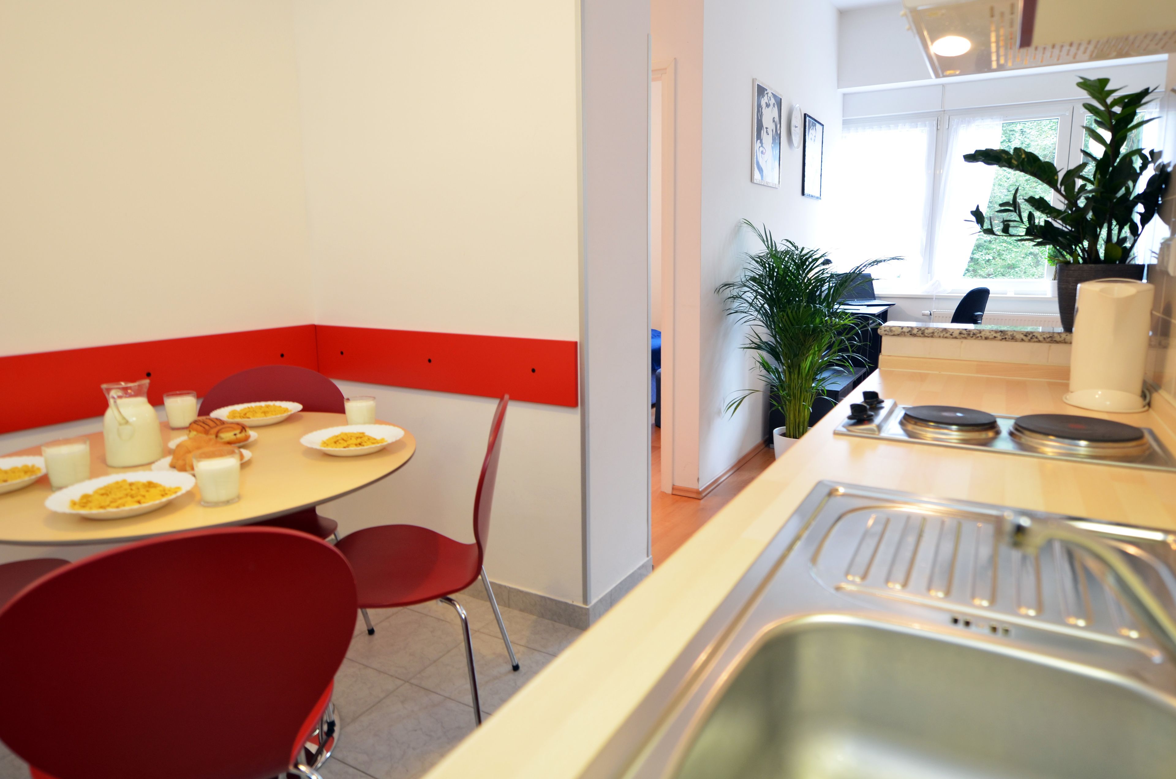 A dining area with a table set for breakfast, red chairs, a sink, and a window with a view of greenery.