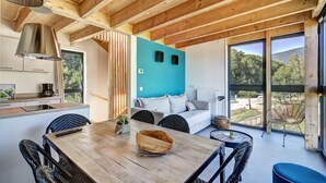 Un intérieur moderne avec un plafond en bois, un coin repas comprenant une table et des chaises, un canapé et une grande fenêtre donnant sur l’extérieur.