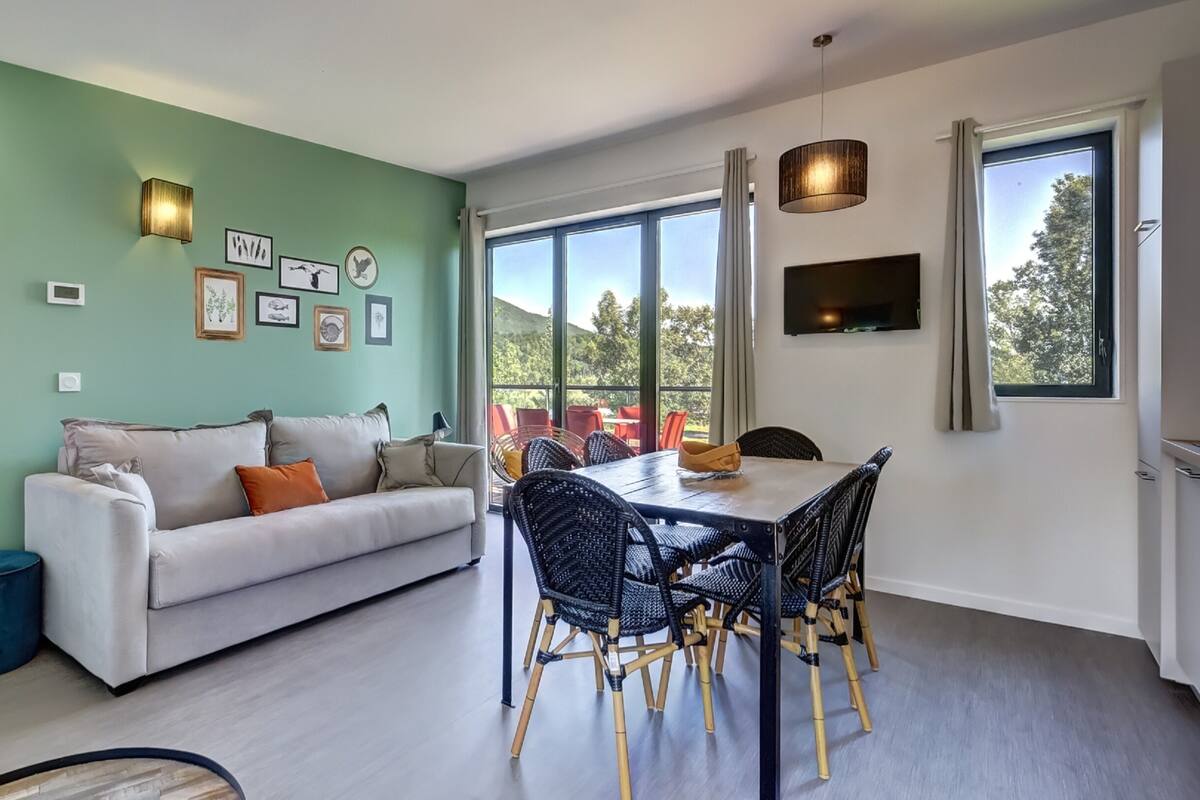 Ein modernes Wohnzimmer mit Sofa, Esstisch und Stühlen, einem großen Fenster mit Blick und Wandbildern.