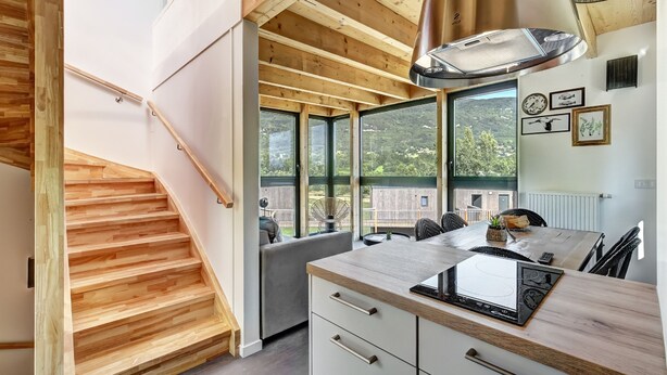 Une cuisine moderne avec des poutres en bois, de grandes fenêtres et une vue sur l’extérieur.