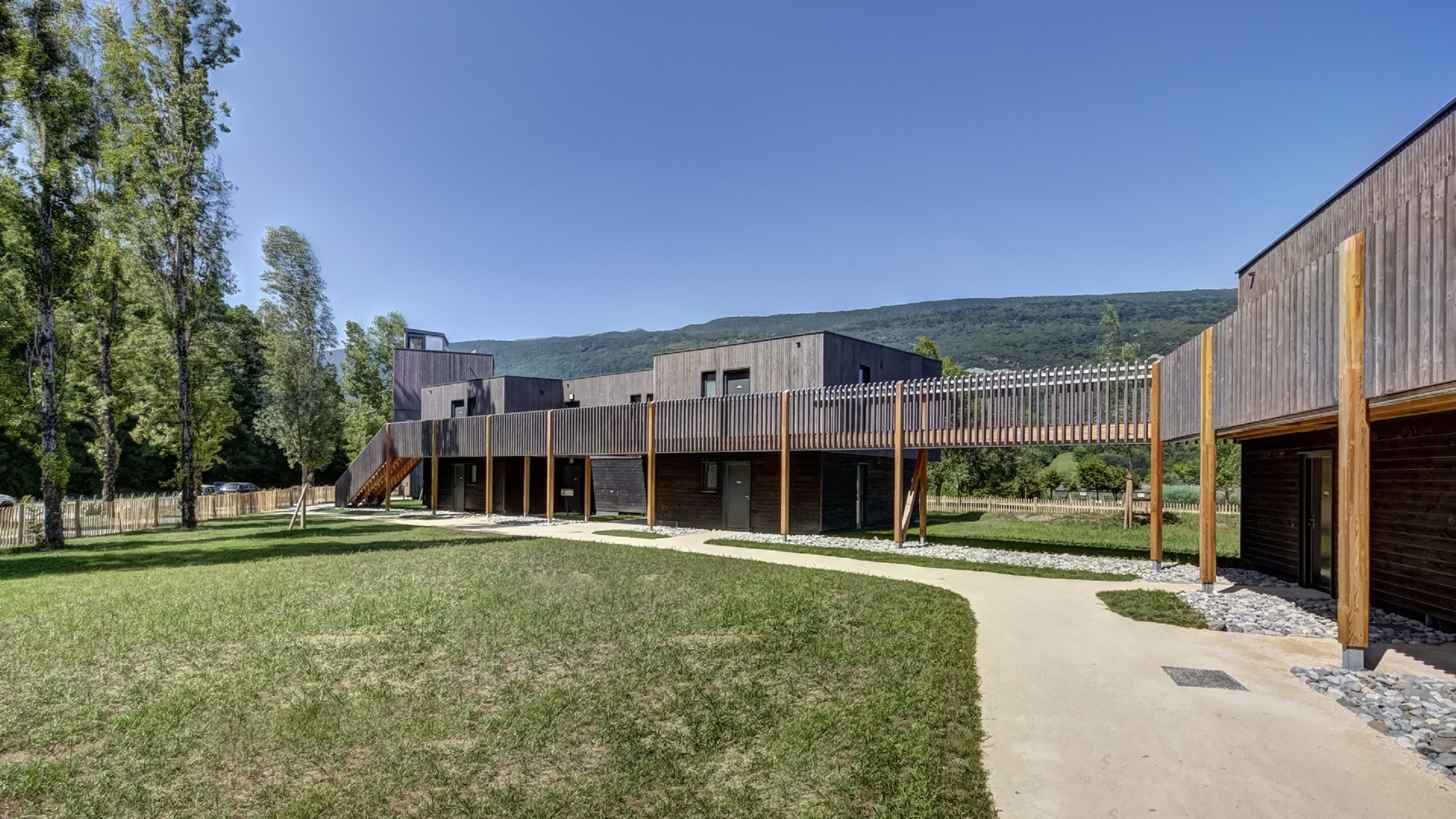 Un bâtiment moderne doté d’un espace extérieur couvert, d’une cour verdoyante et d’une clôture en bois.
