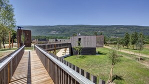 Une terrasse en bois mène à un bâtiment moderne qui offre une vue sur des collines verdoyantes.