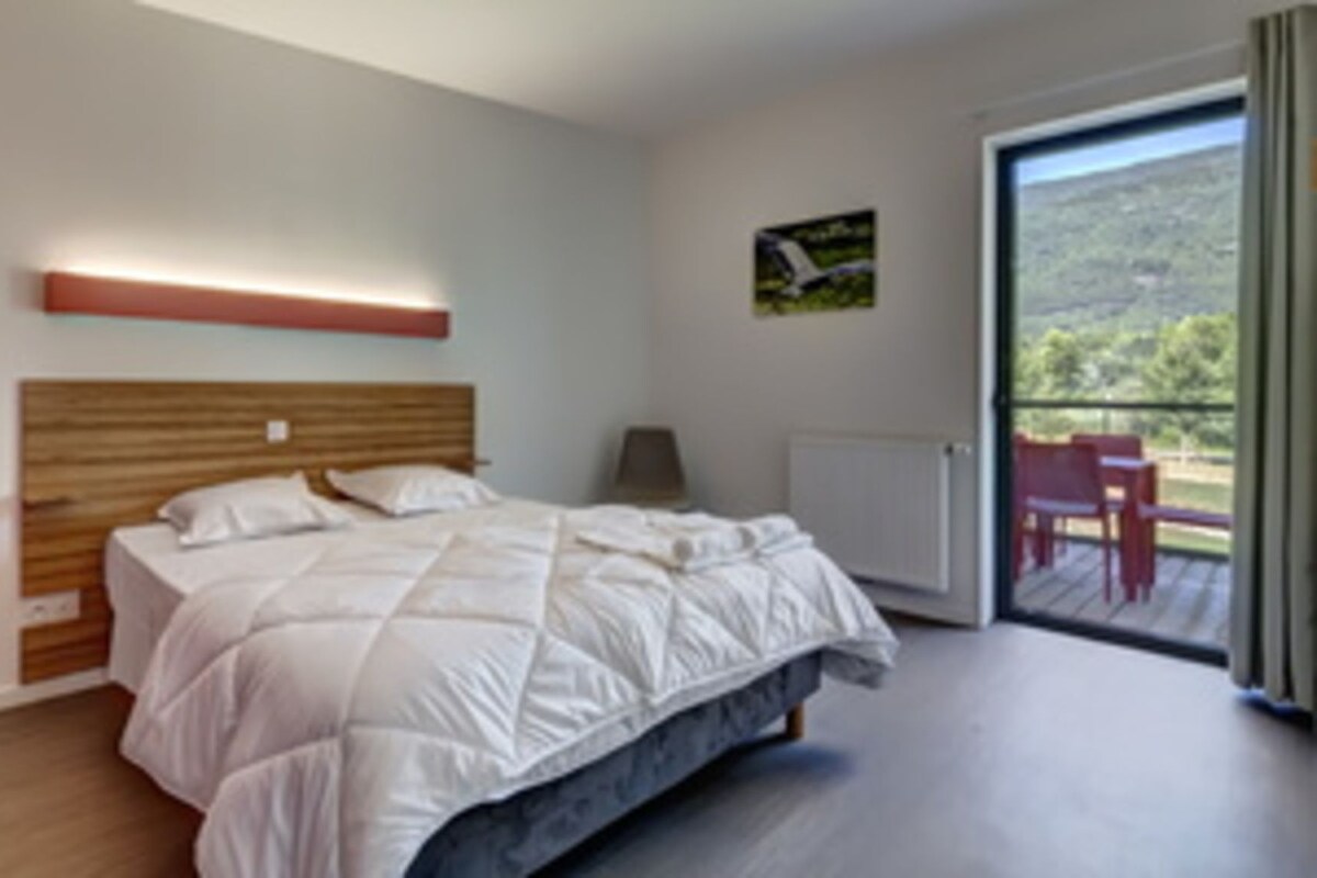 Une chambre à coucher avec un lit, une table de chevet, une fenêtre et une vue sur l’extérieur.