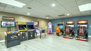 Une salle d’arcade proposant divers jeux de course et jeux d’arcade, notamment un jeu Pac-Man et un jeu de course de NASCAR.