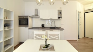 A modern kitchen with white cabinetry, a built-in oven, and pendant lighting. - First Choice Centar - Primorska (Zagreb)