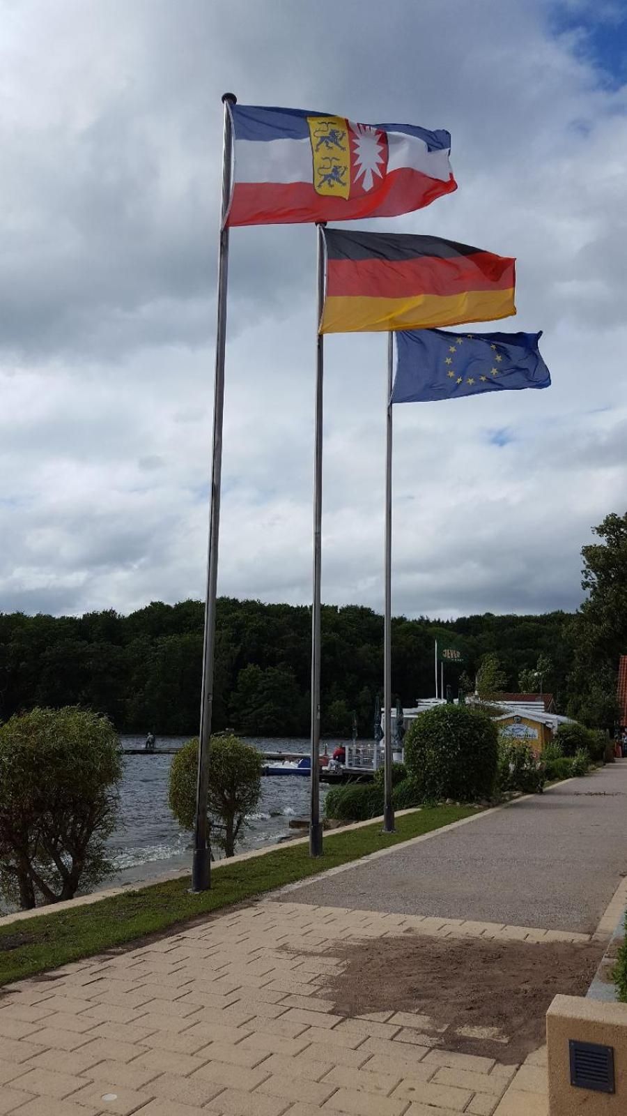 Two flags on flagpoles, a body of water, and a pathway leading to a building.
