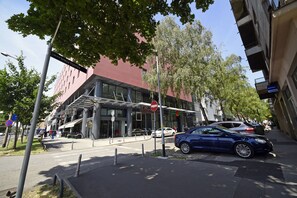 Een modern gebouw met een glazen gevel, een blauwe auto geparkeerd ervoor en een verboden toegang-bord.