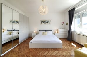 Een moderne slaapkamer met een groot bed, een spiegel, nachtkastjes en een decoratieve lamp.