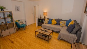A living room with a sofa, a coffee table, a bookshelf, and a lamp. - Lancaster Apartment - Central Tenby (Tenby)