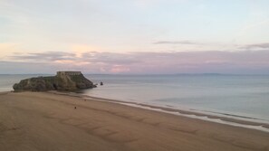 A beach with a rocky outcrop and a building on top. - Lancaster Apartment - Central Tenby (Tenby)