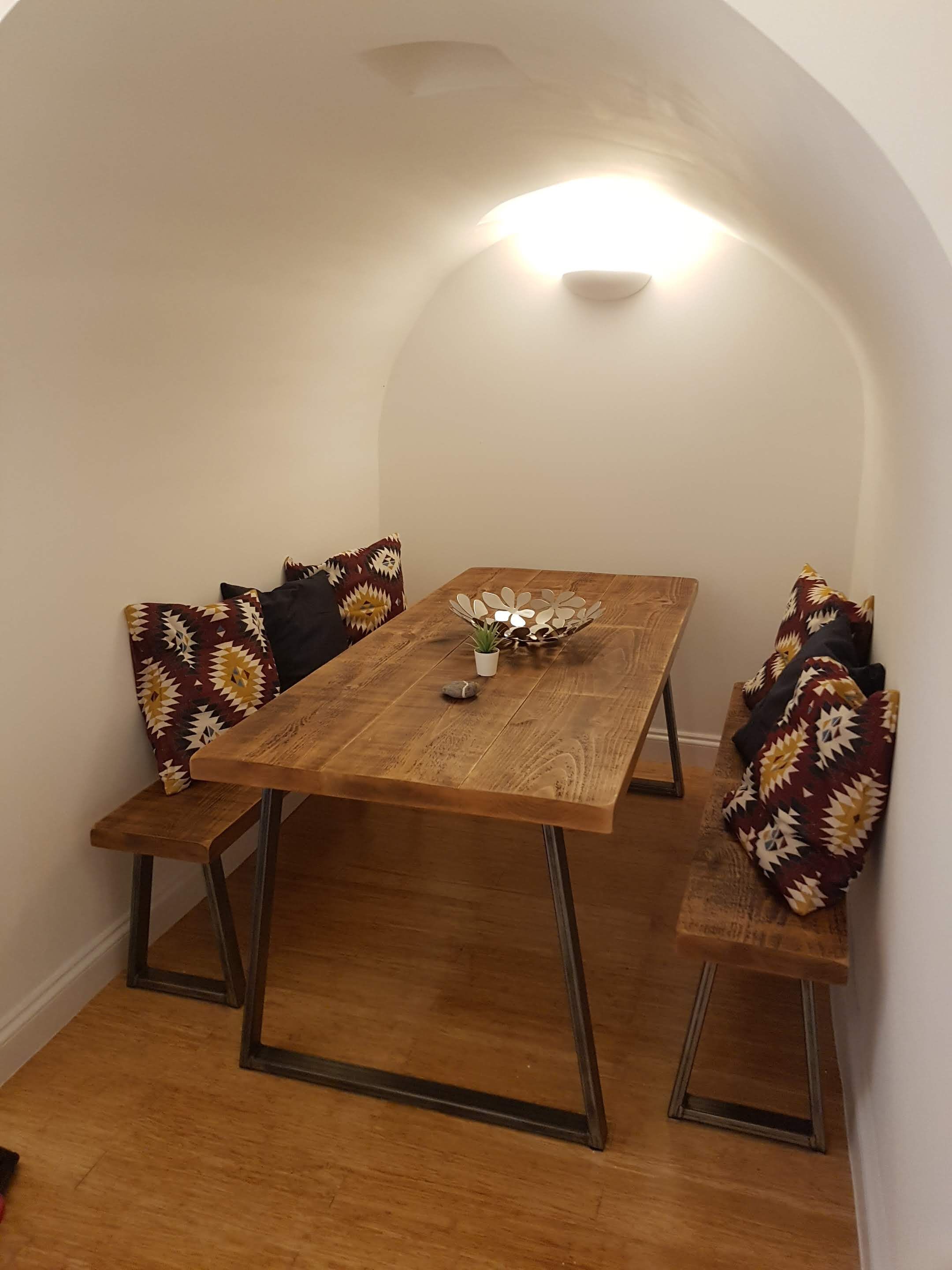 A dining area with a wooden table, benches, patterned cushions, and a decorative centerpiece.