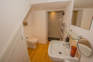 A bathroom with a toilet, sink, and shower. - Lancaster Apartment - Central Tenby (Tenby)