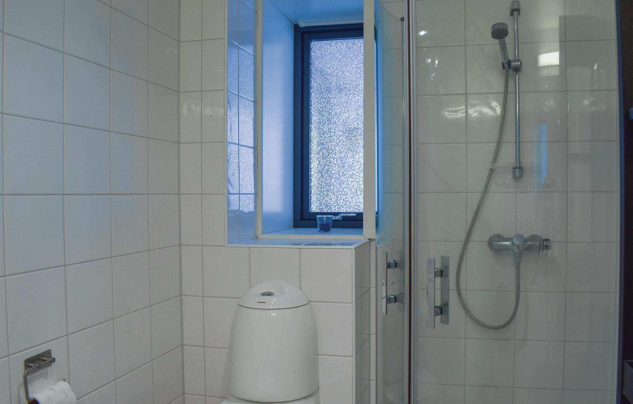 Een badkamer met witte tegels, een toilet, een raam met uitzicht en een douchecabine.