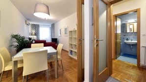 A modern living room with a dining table and chairs, a red sofa, and a large window. - Botanic Apartment (Zagreb)
