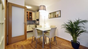 A dining area with a table and chairs, a potted plant, a hanging light fixture, and a kitchen in the background. - Botanic Apartment (Zagreb)