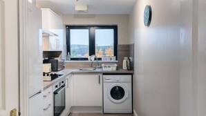 Une petite cuisine étroite avec un lave-linge, une fenêtre et une horloge au mur.