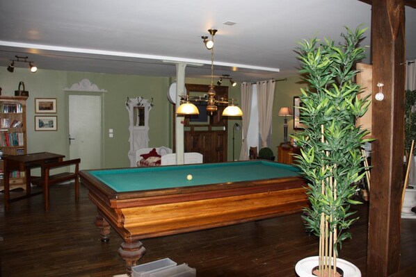 A pool table in a room with wooden flooring, a bookshelf, and a potted plant. - Moulin de la Beraudaie (Bohal)