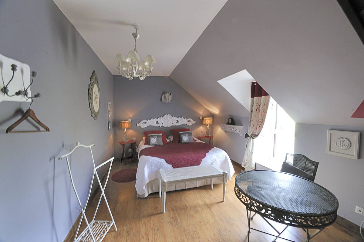 A bedroom with a bed, bedside tables, a hanging light fixture, a chair, and a table.