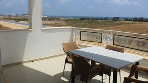 A balcony with a table and chairs, overlooking a coastal landscape with buildings and a road. - Dar Lebharr (Kelibia)