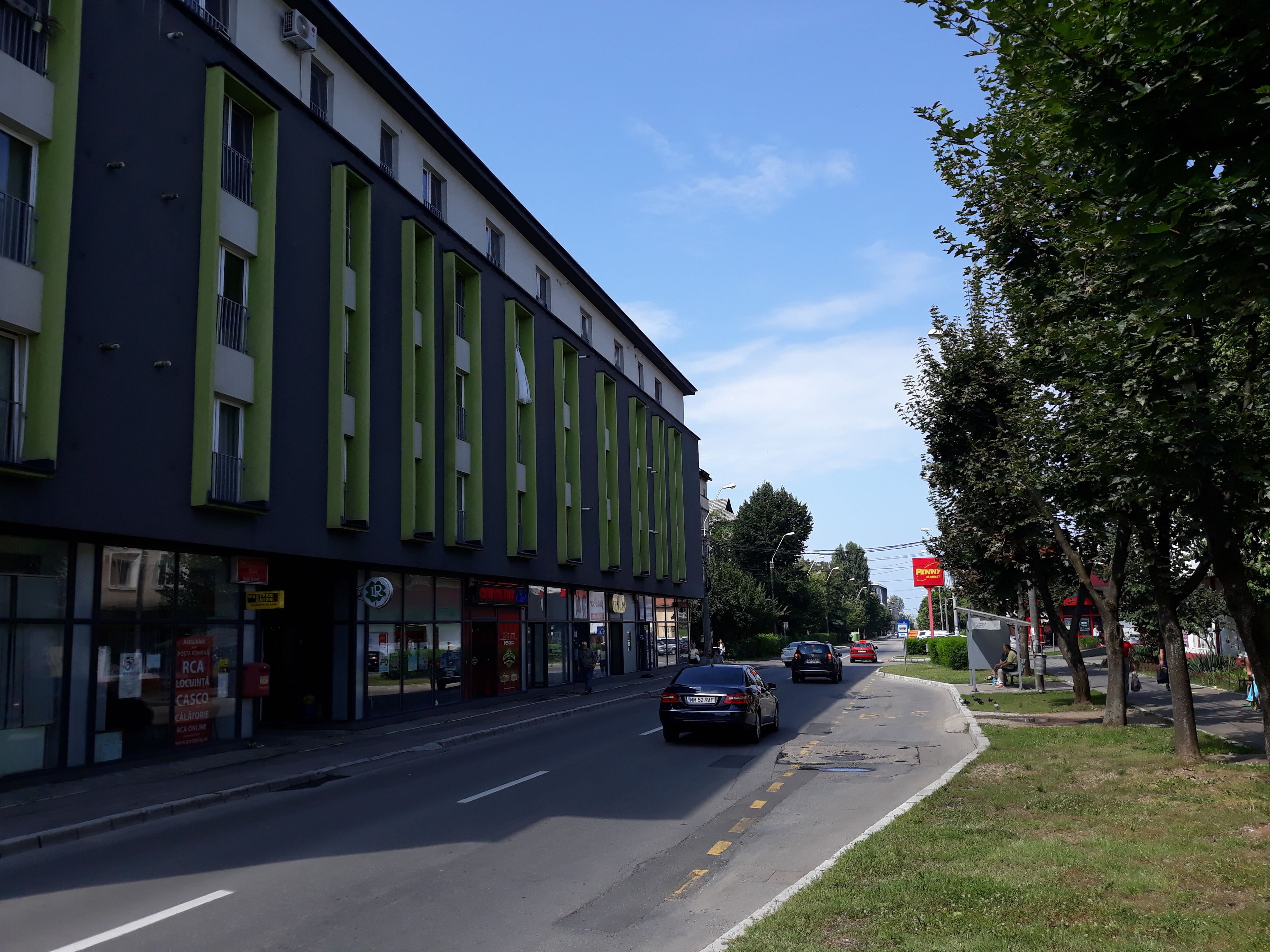 Vista de la calle con un edificio que tiene ventanas amplias y un toldo verde.