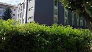 A modern building with a dark facade and green accents, surrounded by lush greenery.