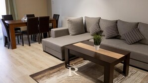 A living room with a sofa, a coffee table, and a dining area with chairs and a table.