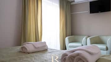 Habitación de hotel con cama, dos sillas, televisor de pantalla plana y ventana con cortinas.
