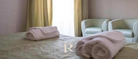 Habitación de hotel con cama, dos sillas, televisor de pantalla plana y ventana con cortinas.
