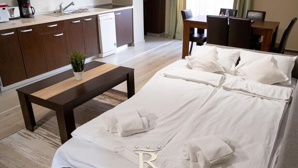 A hotel room with a bed, bedside table, and a small kitchen area with a coffee maker and a plant.