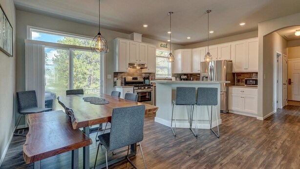 A modern kitchen with white cabinets, a central island with bar stools, and a dining area with a wooden table and chairs.