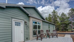 A house with a green exterior, a front door, a window with shutters, and a deck with four chairs.