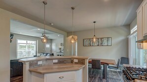 A modern kitchen with a central island, pendant lighting, and a dining area with a view.