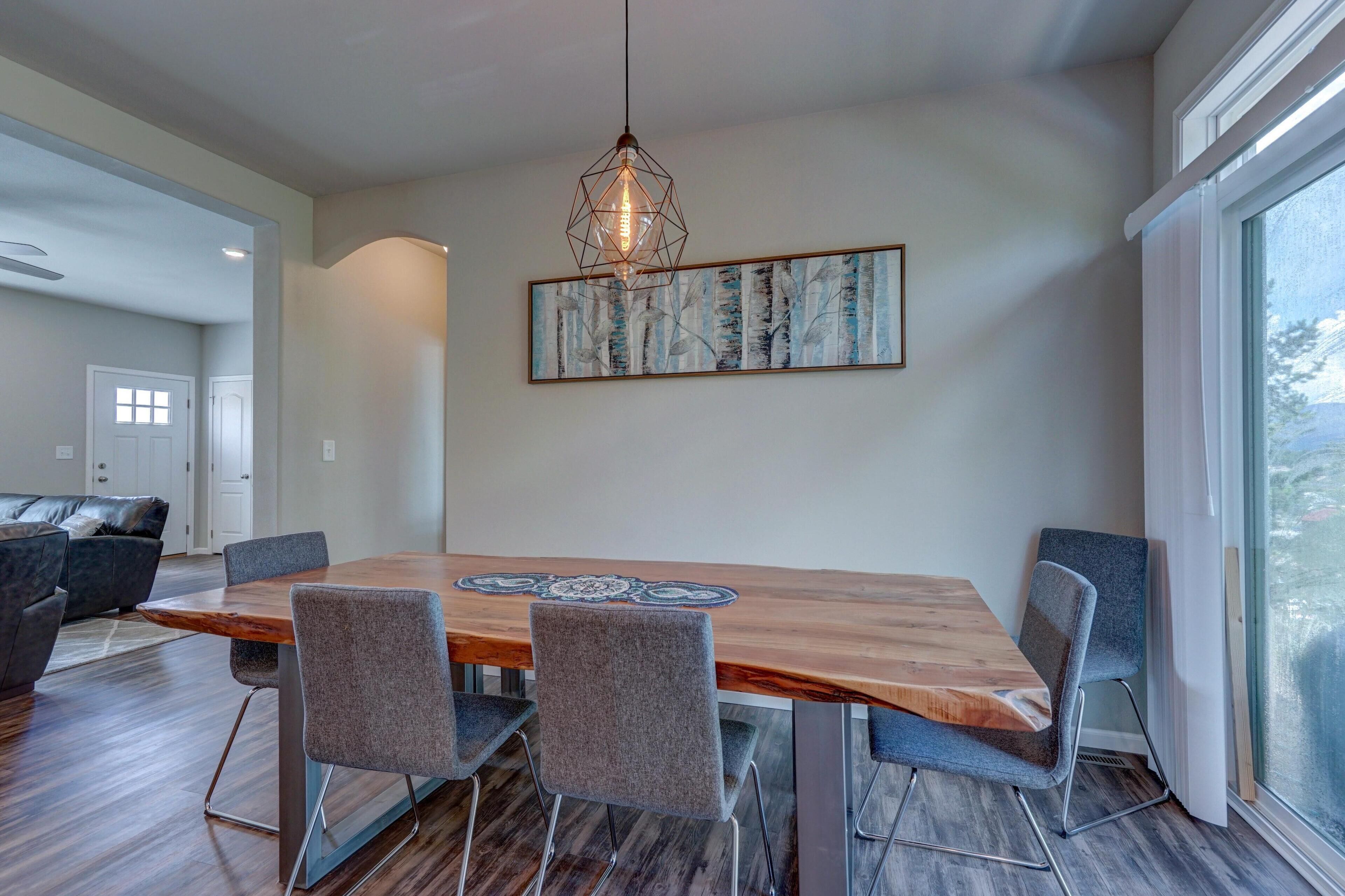 Un comedor con una mesa de madera, cuatro sillas grises, una lámpara colgante y un cuadro abstracto grande en la pared.