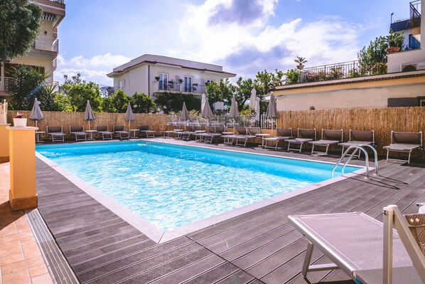 A rectangular swimming pool with lounge chairs and umbrellas, surrounded by a wooden deck. - Hotel Isabella (Sant'Agnello)