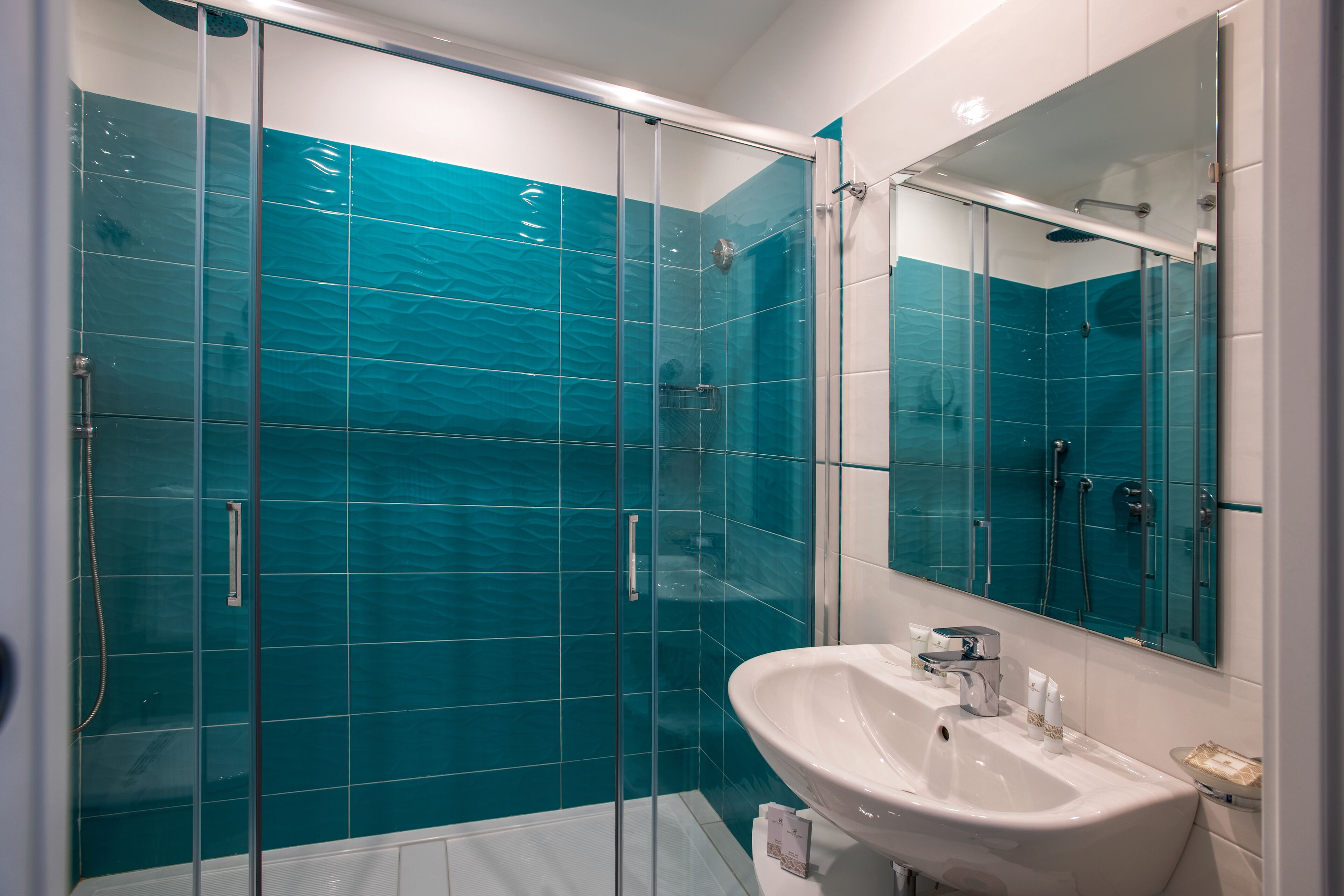 Un bany modern amb dutxa amb envàs de vidre, un lavabo blanc i un mirall gran.