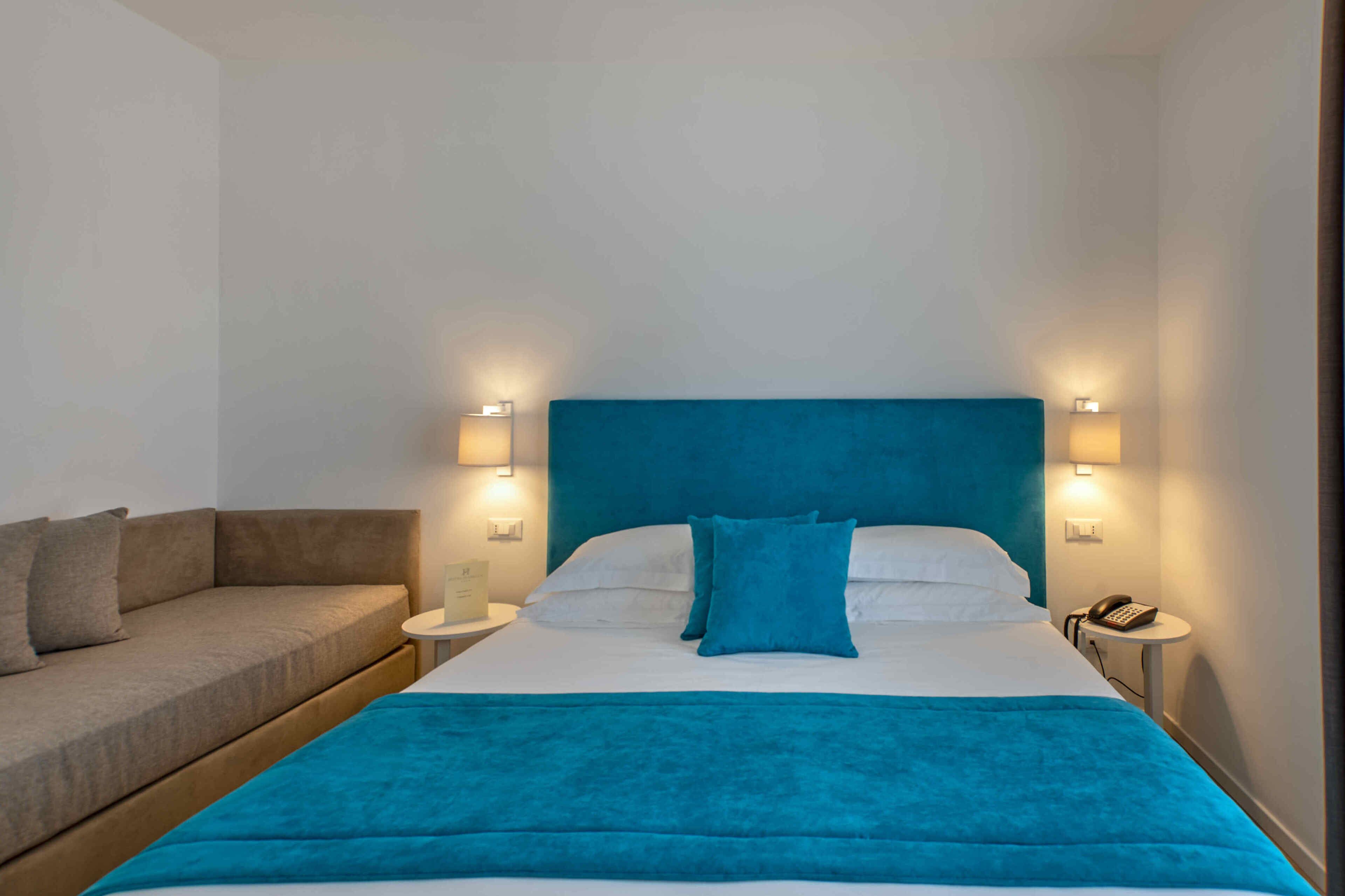 A hotel room with a bed, a sofa, and two bedside lamps.